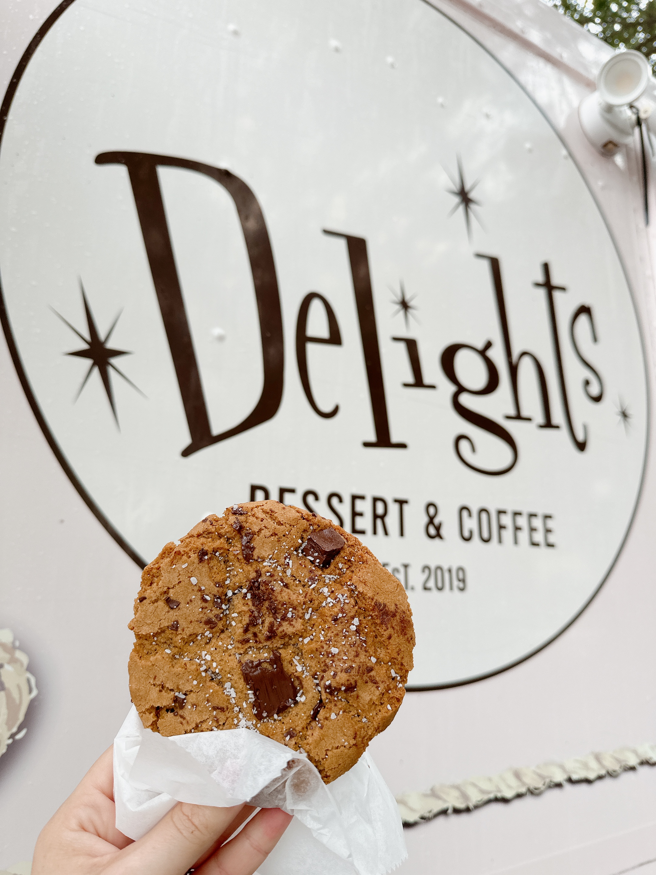 Fresh chocolate chunk sea salt cookie held up in front of the Delights truck logo